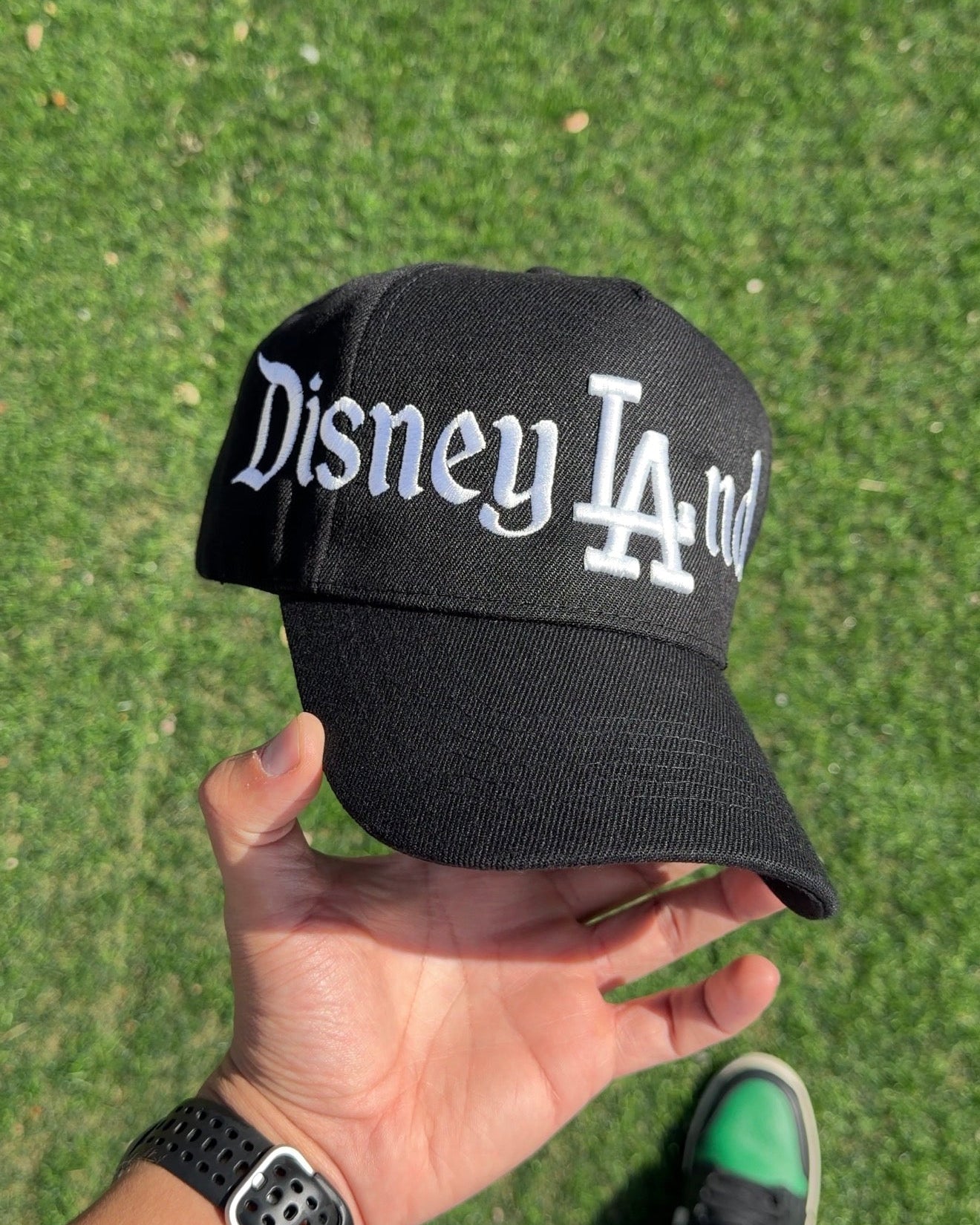 Black cap with 'Disney LA' text held by a person on grass